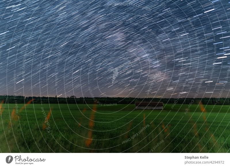 Startrails über eine kleine Hütte auf einem Acker bei sternenklarer Nacht, schöne Natur und Konzept für Bewegung der Erde. Startschienen Haus Ackerland Himmel