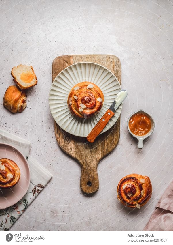 Teller mit Zimtschnecke bei Marmelade Brötchen Dessert dienen Messer Sahne Schneidebrett Serviette Frühstück lecker frisch Lebensmittel Schalen & Schüsseln