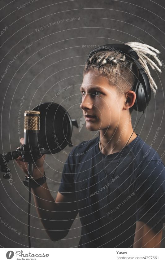 Vertikaler Schuss stilysh Kerl mit Dreadlocks ist die Aufnahme eines Songs im Studio. Eine junge attraktive Sängerin mit schwarzen Studiokopfhörern steht vor einem Mikrofon und singt. Generation Z junges Talent