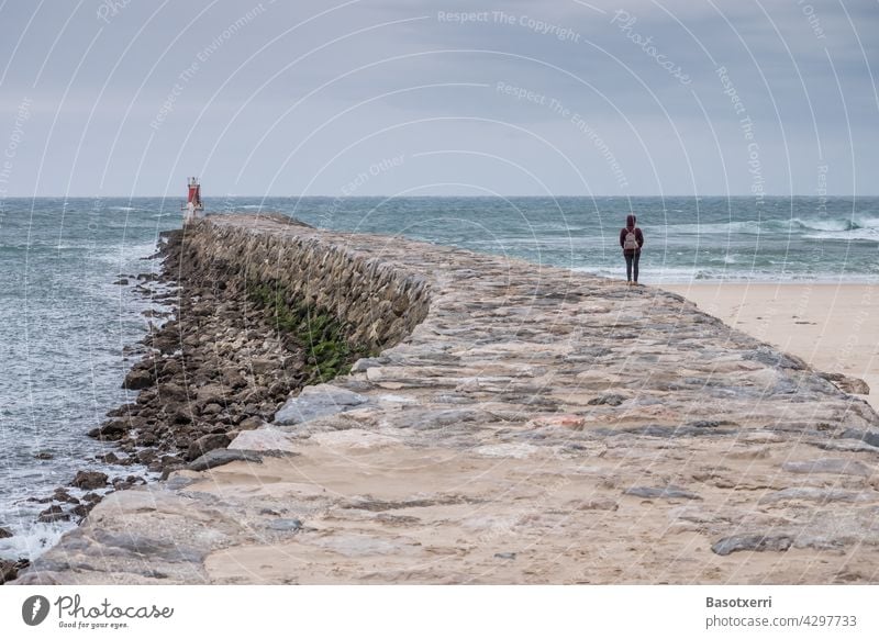 Graues ungemütliches Wetter auf der Mole - eine Reisende blickt auf das Meer. San Vicente de la Barquera, Kantabrien, Spanien Ozean Wasser Wellen Frau reisen