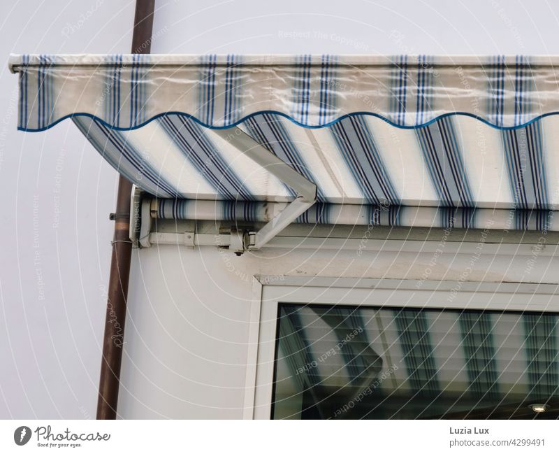 Streifen und Streifen: eine Markise spiegelt sich im Fenster. Im Raum dahinter ist es dunkel, aber es brennt noch Licht. Schaufenster Lampe Spiegelung weiß blau