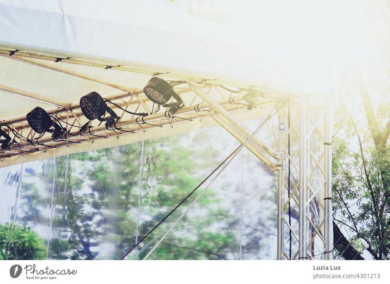 Bühnendach mit Scheinwerfern vor blauem Sommerhimmel, Sonnenschein und grünem Laub hell hoch sommerlich Licht Musik Show Konzert Open Air weiß Bäume Baumwipfel