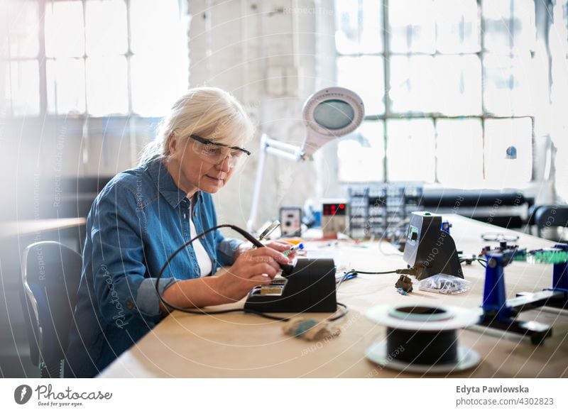 Seniorin in der Elektronikwerkstatt Messung aktuell Elektrizität Elektromonteur Ingenieur Gerät Kompetenz Industrie Job Reparatur Lötkolben löten