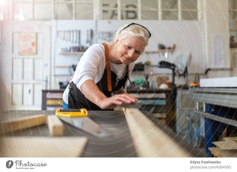 Ältere Frau bei Holzarbeiten in einer Werkstatt im Innenbereich Mechaniker Besitzer Beruf Dienst Kleinunternehmen Mitarbeiter Techniker Arbeitsplatz Arbeiter