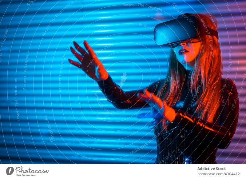 Junge Frau erkundet virtuelle Realität VR erkunden interagieren Headset gestikulieren eintauchen neonfarbig leuchten futuristisch jung Schutzbrille Innovation