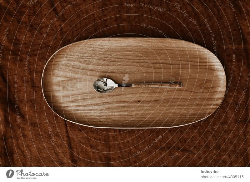 Ein Metalllöffel mit Holzgriff auf einem Holztablett auf dunkelbraunem Textilhintergrund. Flachlage, Ansicht von oben. Löffel Utensil Besteck hölzern Holzplatte