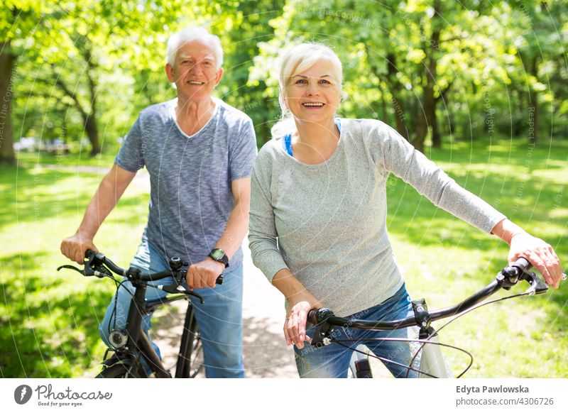 Senior Paar Reiten Fahrräder im Park Fahrrad Zyklus Senioren Rentnerin Rentnerinnen lässig im Freien Tag Kaukasier Fröhlichkeit zahnfarben Lächeln genießend