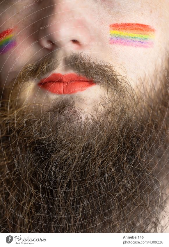 Junger gut aussehender bärtiger Mann mit Stolzflagge auf der Wange, Regenbogenflagge steht für LGBTQ, Gender-Recht und sexuelle Minderheit. Porträt Fahne lgbt