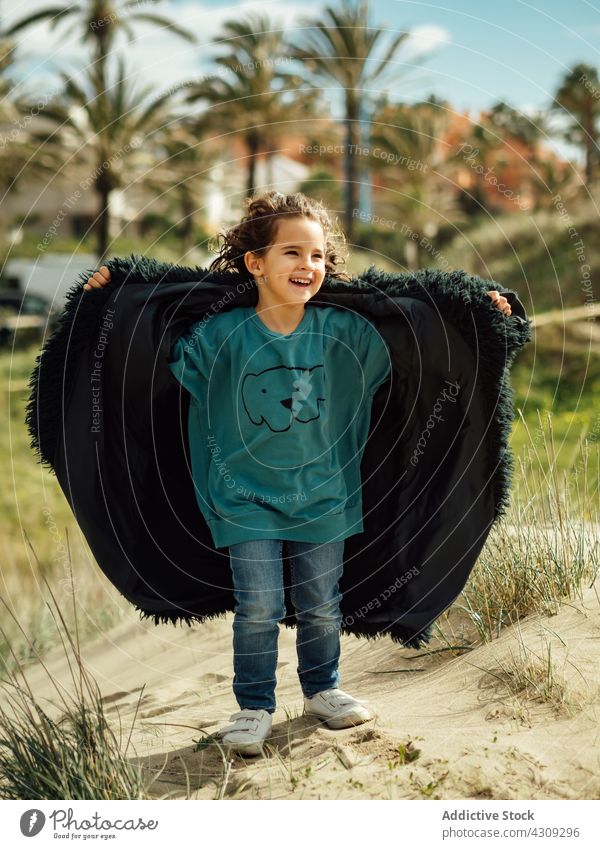 Fröhliches Kind im Pelzmantel am Sandstrand stehend Mädchen Strand Glück heiter Wind Fell Mantel Natur frisch Lachen wenig niedlich Kindheit Ufer Küste sonnig