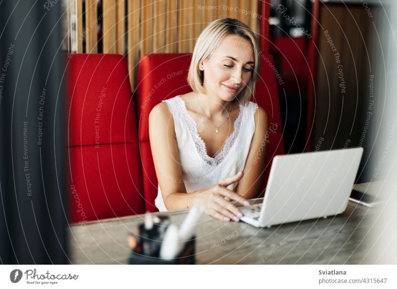 Ein schönes blondes Mädchen benutzt einen Laptop und arbeitet in einem Café. Pause, online arbeiten, freiberuflich benutzend Computer Arbeit Internet Business