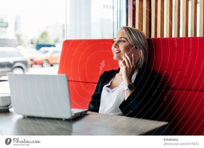 Ein attraktives Mädchen spricht mit einem Mobiltelefon und lächelt, sitzt allein in einem Café Telefon sprechend Frau Sitzen Tablette Geschäftsfrau Business