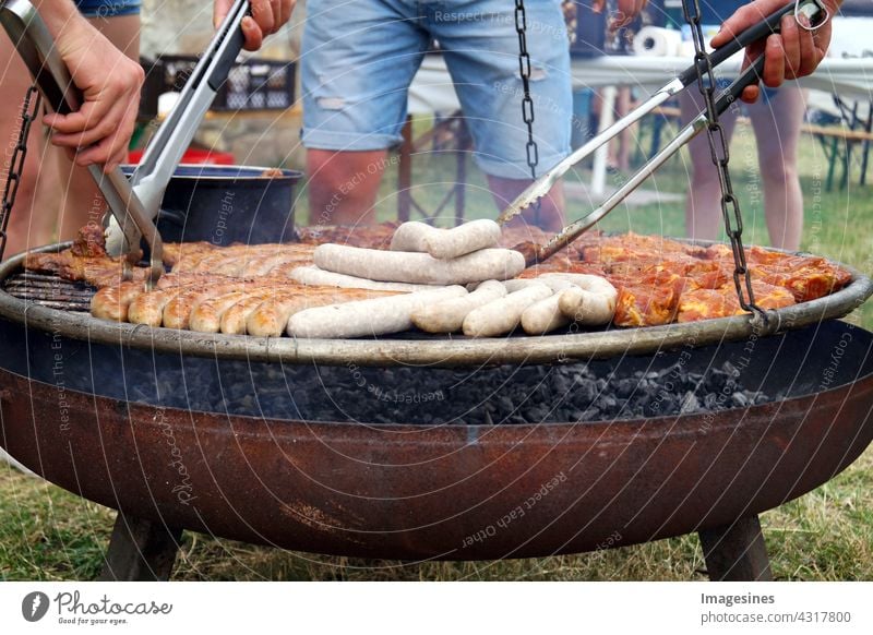 Barbecue - geselliges Beisammensein. Bratwurst und gegrilltes Fleisch, Steaks über den Kohlen auf dem Grill. Männer in kurzen Jeans grillen über einem Grillfeuer eine Auswahl an Fleisch- und Wurstwaren.