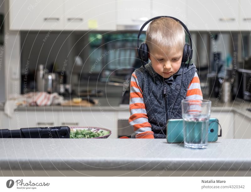 Kleines Kind Junge wares Kopfhörer und spielen das Handy auf dem Küchentisch Computer Sohn Tablette studierend Koch Haus Internet Technik & Technologie