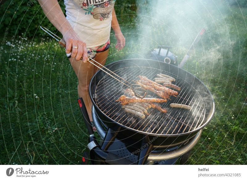 Grillen am Holzkohlengrill mit Bratwürsten und rauchenden Holzkohlen Grillsaison Kugelgrill Grillplatz Feuer Sommer Essen Glut Grillkohle Rauch gegrillt