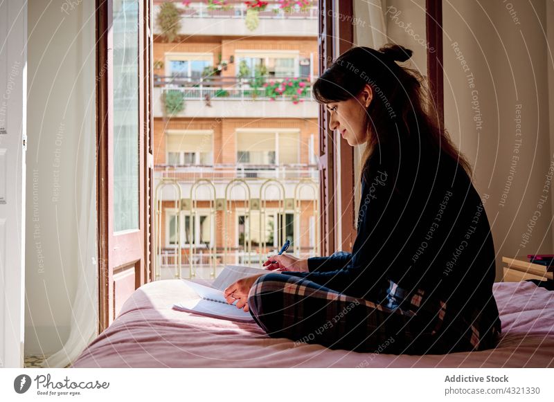 Fröhliche Frau mit Notizbuch auf dem Bett Schüler Bildung Hausaufgabe lernen heimwärts Notebook Notizblock Lächeln Anweisung Universität Glück Wissen heiter