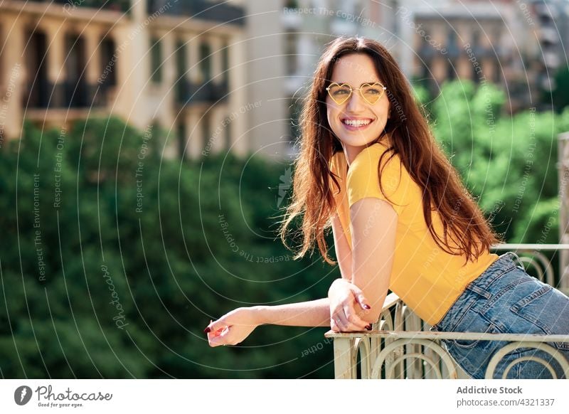 Glückliche Frau mit Sonnenbrille auf dem Balkon stehend Sommer gelb Farbe hell heiter Lächeln trendy Stil Terrasse Freude charmant Optimist Outfit Brille