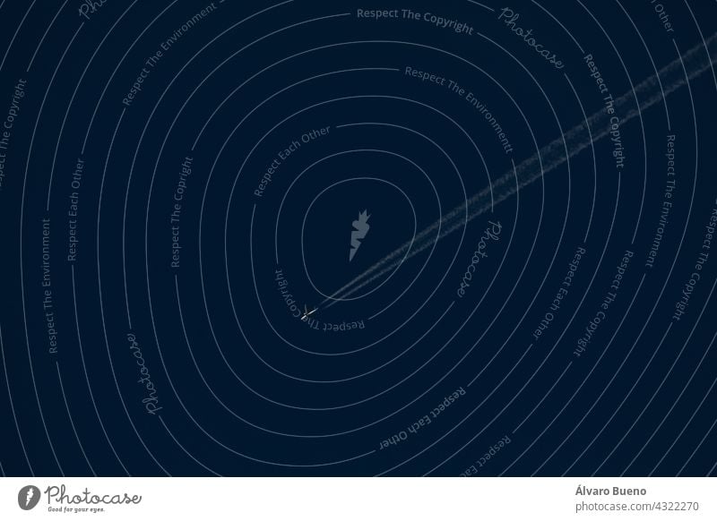 Ein weißes Passagierflugzeug fliegt in der Ferne durch einen dunkelblauen Himmel und hinterlässt eine Spur aus weißem Rauch und Dunst, Spanien Flugzeug