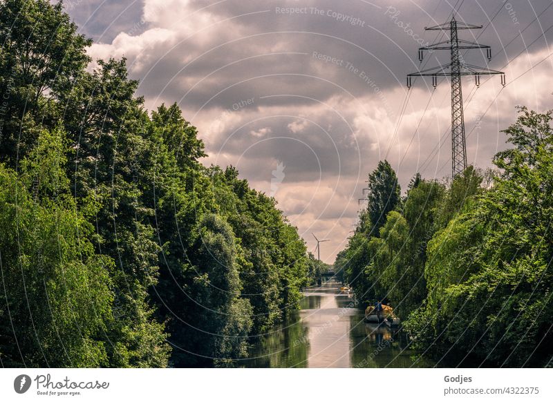 Fluß zwischen grünen Bäumen mit Blick auf Windkraftanlage und Strommast, Energiewende Natur Elektrizität Hochspannungsleitung Bootsfahrt Energiewirtschaft