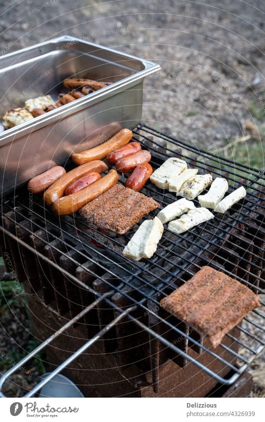 Würstchen grillen auf heißen Kohlen im Freien, zwei Grills mit Fleisch, Käse und Würstchen Haloumi haloumni gegrillter Käse Barbecue Zange tong Wurstwaren