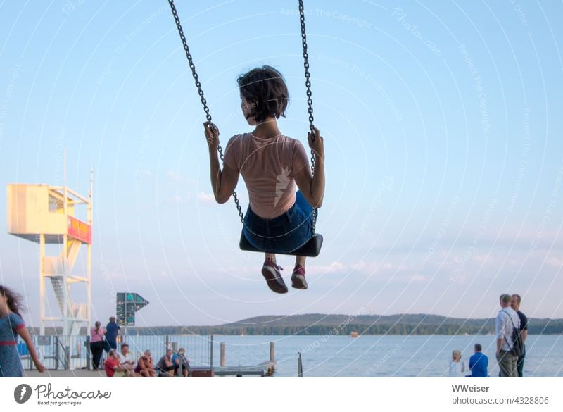 Auf der Schaukel erlebt das Mädchen Schwung und Leichtigkeit. Auch die anderen Menschen am See genießen den Feierabend schaukeln Spaß verspielt bunt Wochenende