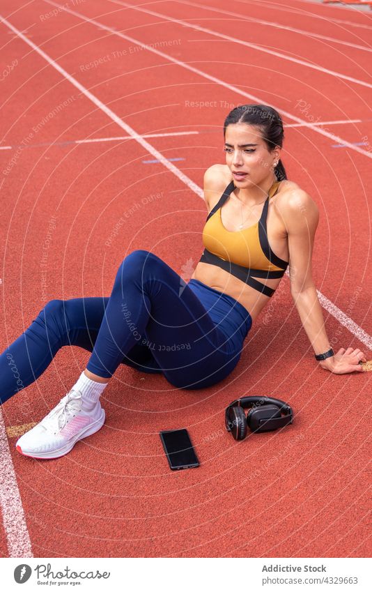 Sportliche Frau macht Pause auf der Stadionbahn Sportlerin Athlet ruhen Bahn Smartphone Kopfhörer Training müde Fitness passen jung Erholung Turnschuh ethnisch