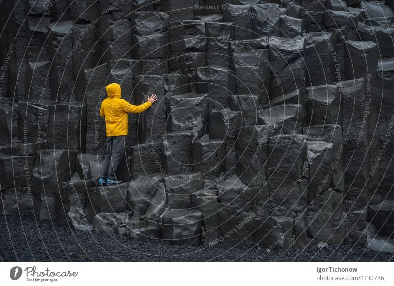 Erwachsener Mann in gelber Jacke steht auf Basaltsäulen am Reynisfjara Black Sand Beach in Island Strand schwarz Stehen Spalten Natur vulkanisch Vik reisen MEER