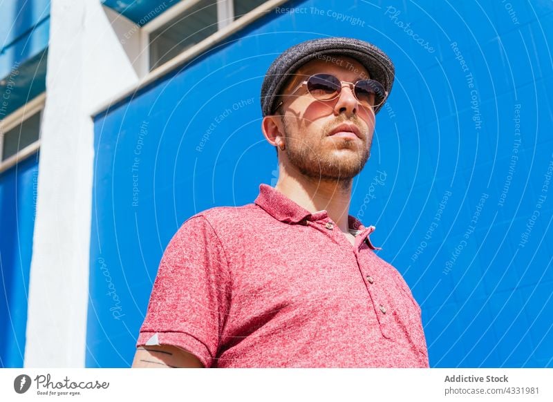 Mann in trendigem Outfit und Sonnenbrille auf blauem Hintergrund Stil Sommer trendy Vollbart urban männlich jung modern Hipster freundlich gutaussehend Polo