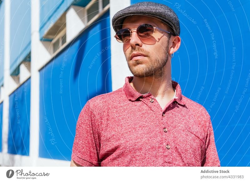 Mann in trendigem Outfit und Sonnenbrille auf blauem Hintergrund Stil Sommer trendy Vollbart urban männlich jung modern Hipster freundlich gutaussehend Polo