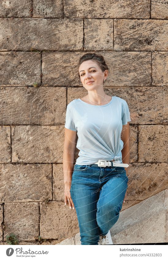 Frauen in T-Shirt und Jeans bleiben in der Nähe einer Wand Erwachsener mittleres Alter Lächeln lässig Attrappe im Freien blondhaarig Jahrtausende Textfreiraum