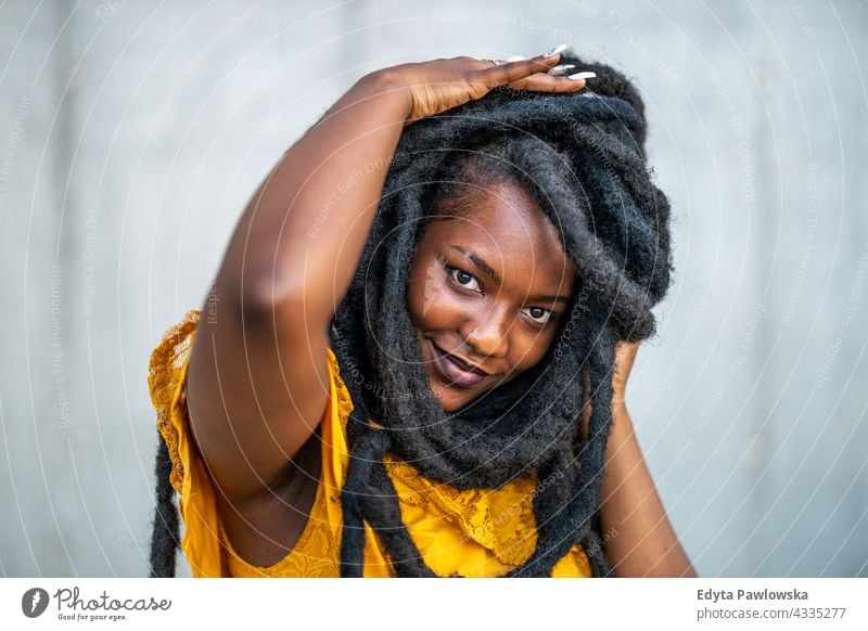 Schöne junge Frau mit Dreadlocks vor einer grauen Wand Rastalocken stolz echte Menschen Stadtleben Afroamerikaner Afrikanisch schwarz Ethnizität sonnig