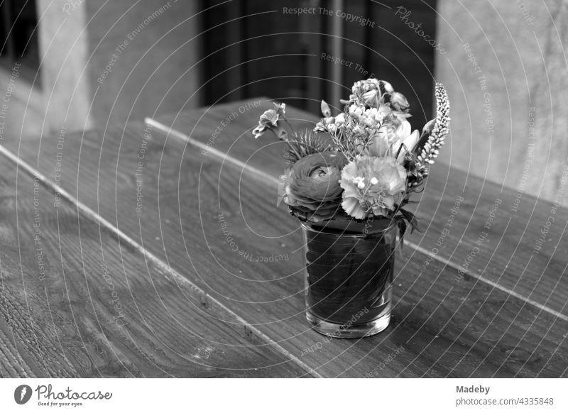 Schlichtes Trinkglas mit Blumenschmuck auf einem Holztisch vor einem Café in der Braubachstraße in Frankfurt am Main in Hessen, fotografiert in neorealistischem Schwarzweiß