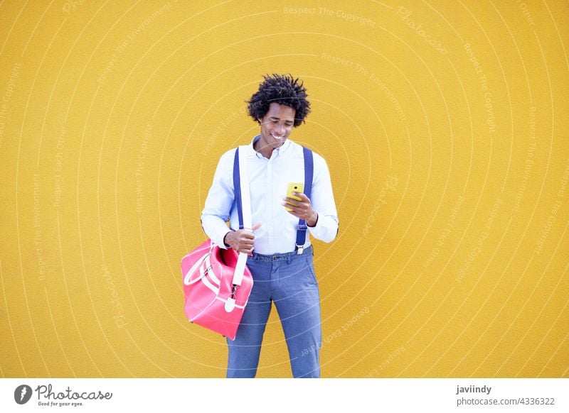 Schwarzer Mann mit Afro-Frisur trägt eine Sporttasche und Smartphone in gelbem Hintergrund. Geschäftsmann schwarz Tasche Business Afro-Look lockig Behaarung Typ