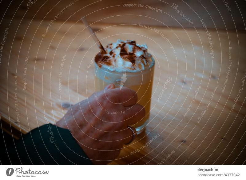 Ein Erfrischungstrink wird gereicht, mit Sahne und Schokopulver, über einen Holztisch. Für den Rest im Glas ist auch ein Strohhalm dabei. trinken Getränk