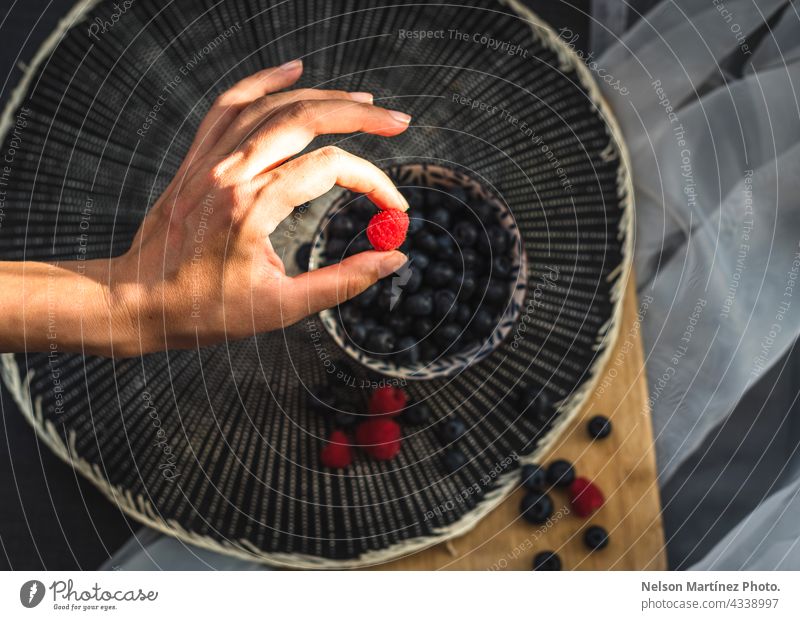 Hand hält eine Himbeere mit einem Teller und Blaubeeren im Hintergrund Snack Nahaufnahme Handvoll organisch Lebensmittelgeschäft Diät Frau Beteiligung