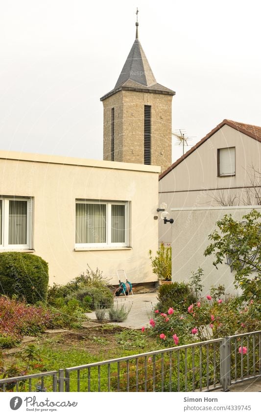 Kirche im Dorf Kirchturm Vorstadt Bungalow Haus Vorgarten Kreuz Flachdach Rosen Gartenzaun Dächerlandschaft Himmel gebüsch Fenster