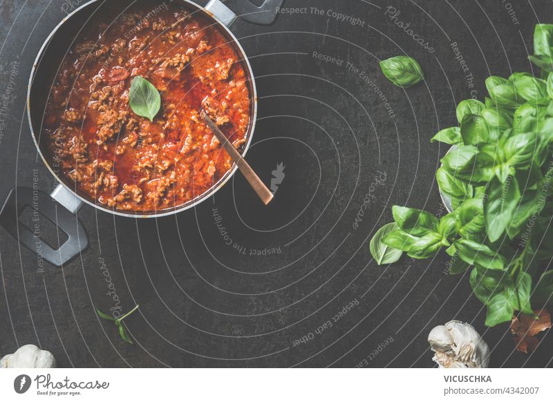 Lebensmittel-Hintergrund mit Sauce Bolognese in schwarzem Kochtopf auf dunklem Hintergrund. Ansicht von oben Bolognesesauce Saucen dunkel Draufsicht