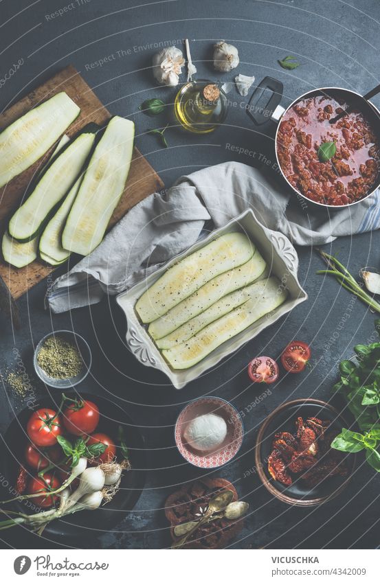 Lecker Low Carb kochen. Lasagne Bolognese mit geschnittenen Zucchini auf dunklem Küchentisch mit Zutaten . Ansicht von oben geschmackvoll Essen zubereiten