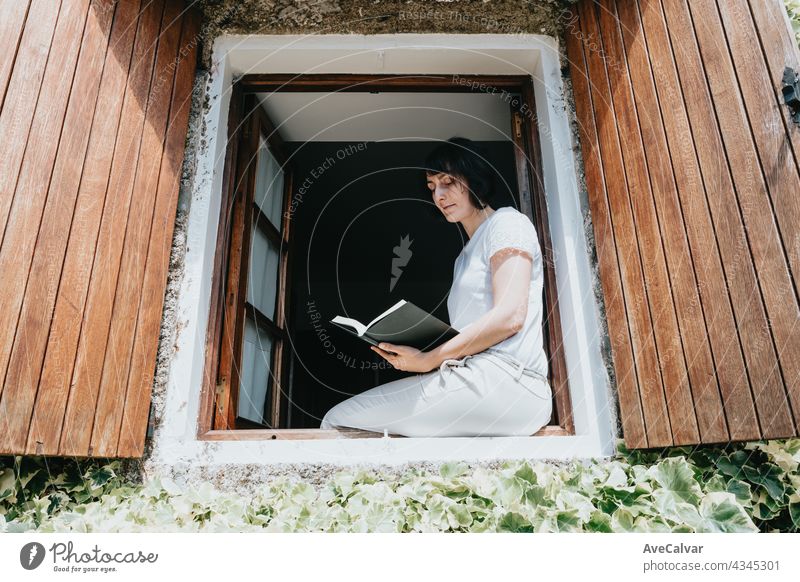 Eine junge Frau mit einem Buch sitzt auf der Fensterbank, Lesen und Entspannen während eines sonnigen Tages Teenager Person Bildung im Innenbereich lesen Raum