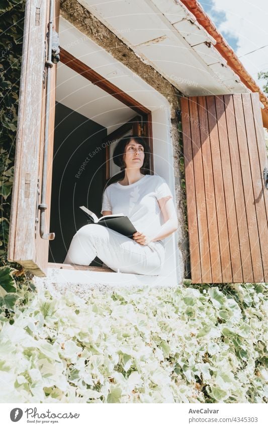 Eine junge Frau mit einem Buch sitzt auf der Fensterbank, Lesen und Entspannen während eines sonnigen Tages Teenager Person Bildung im Innenbereich lesen Raum