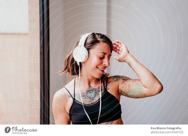 glückliche muskulöse kaukasische Frau, die Musik auf dem Handy und Headset in der Turnhalle hört. Tanzen am Fenster während der Tageszeit. Sport und gesunder Lebensstil