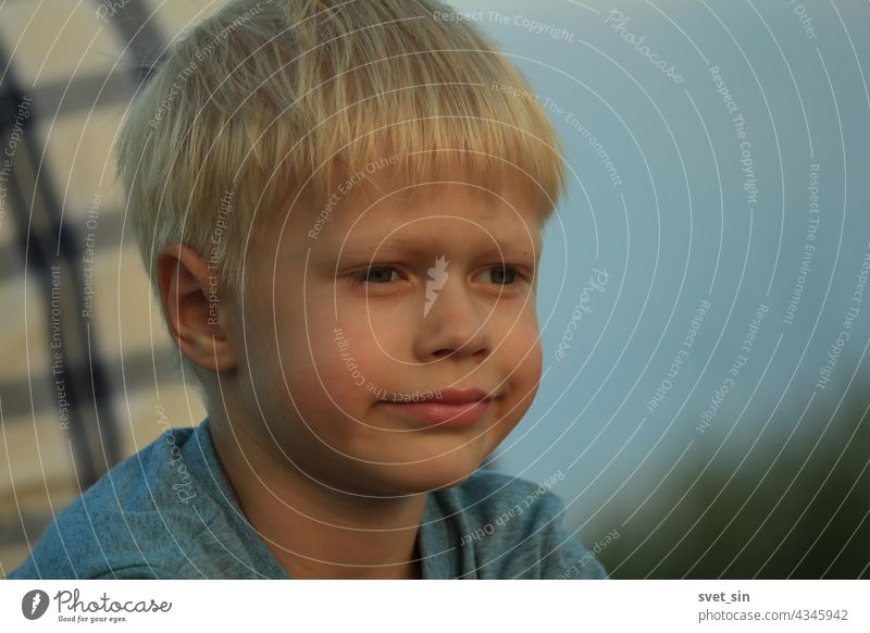 Porträt eines nachdenklichen blonden Jungen vor dem Hintergrund eines Männerrückens in einem karierten Hemd und blauem Himmel an einem Sommerabend im Freien.