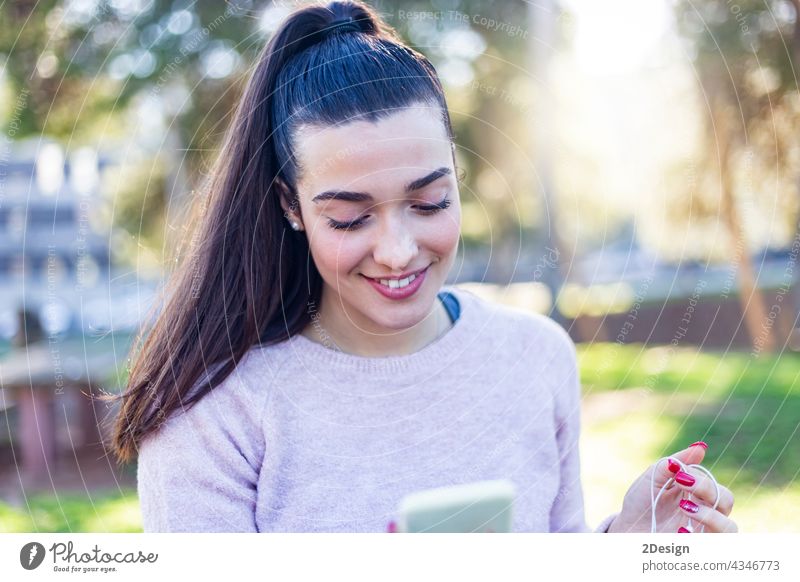 Schönes Mädchen sitzt auf einer Bank Brünette in einer lässigen Kleidung, Mode Lebensstil mit einem Telefon. Attraktive junge weibliche Chatten auf Handy. mit Smartphone