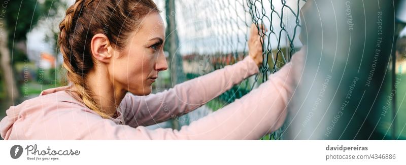 Seriöse Hafenarbeiterin mit Boxerzöpfen, die an einem Metallzaun lehnt ernst Frau Sportlerin Boxerflechten Lehnen Profil Transparente Netz Kopfball Panorama