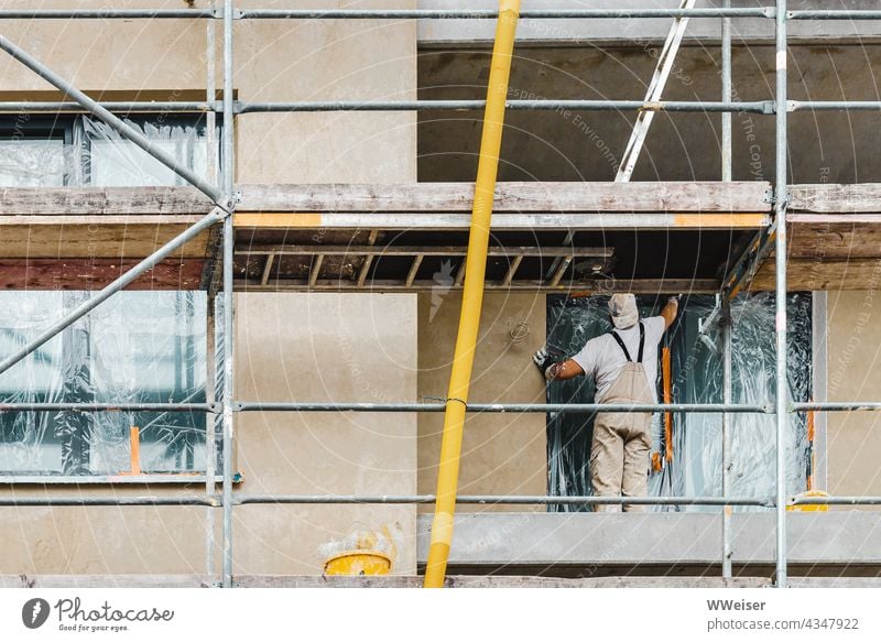 Ein Bauarbeiter klebt die Fenster mit Folie ab, er will die Fassade streichen Baustelle Arbeit Haus Bauarbeiten Renovierung Sanierung Restauration maler