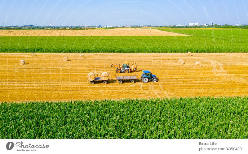 Blick von oben auf ein landwirtschaftliches Feld, das Rundballen aus Stroh sammelt Antenne Ackerbau Ballen Ladung führen Müsli bedeckt umhüllt Bagger Landwirt