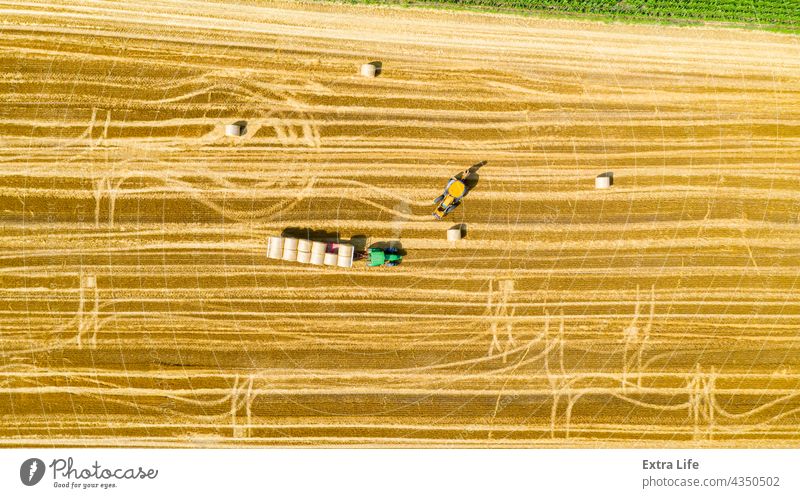 Blick von oben auf ein landwirtschaftliches Feld, das Rundballen aus Stroh sammelt Antenne Ackerbau Ballen Ladung führen Müsli bedeckt umhüllt Bagger