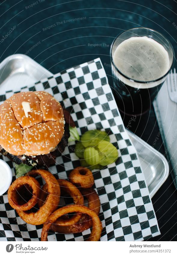 Blauschimmelkäse-Bacon-Burger mit Zwiebelringen auf einem Riffelteller Amerikaner Hintergrund Speck Barbecue Rindfleisch Bier bleu Brot Brötchen kariert Käse