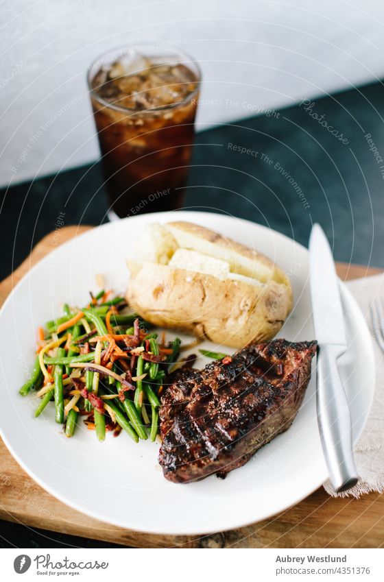 klassisches Steak- und Kartoffelessen mit einer Limonade vor einem schwarz-weißen Hintergrund angus Ofenkartoffel Barbecue grillen Rindfleisch Holzplatte