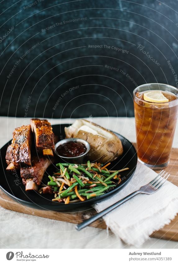 Abendessen mit Rippchen, grünen Bohnen und Kartoffeln vor einem modernen schwarzen Hintergrund Amerikaner gebacken Ofenkartoffel Barbecue gegrillt grillen