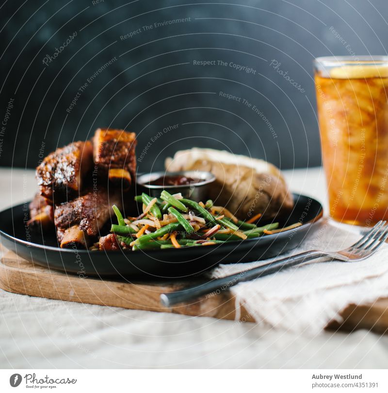 Rippchen mit grünen Bohnen und Kartoffeln auf einer Tischdecke aus Leinen im Landhausstil Amerikaner Hintergrund gebacken Ofenkartoffel Barbecue gegrillt